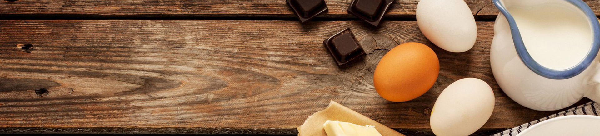 Carrés de chocolat, ouufs, et une plaquette de beurre posés sur des planches en bois